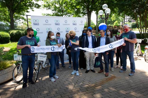 Ribbon cutting for bike share station. A group of people hold a long ribbon