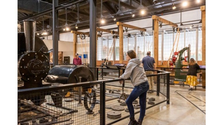Young woman leans on fence around museum display of machinery