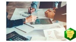Photograph of three sets of hands working with a touchpad and calculator, documents and graphs on table before them